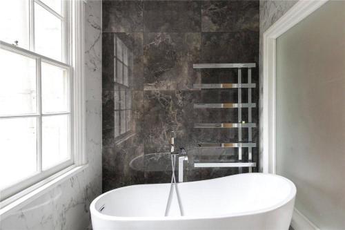 4 Bedroom Townhouse Seconds Away from Harrods في لندن: حوض استحمام أبيض في حمام مع نافذة