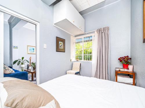 1 dormitorio con cama blanca y ventana en Cosy Victorian Style Full Apartment, en Ciudad del Cabo
