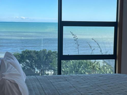 a bedroom with a view of the ocean through a window at Absolute Beachfront Holiday Home With Private Beach Access To Swim Beach Spectacular Sunsets in Paraparaumu