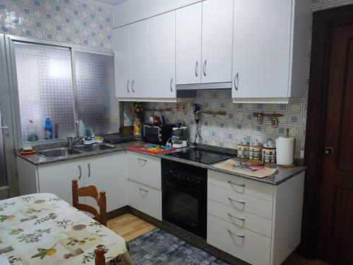 una cucina con armadi bianchi, lavandino e tavolo di Casa Jesús a Sarria
