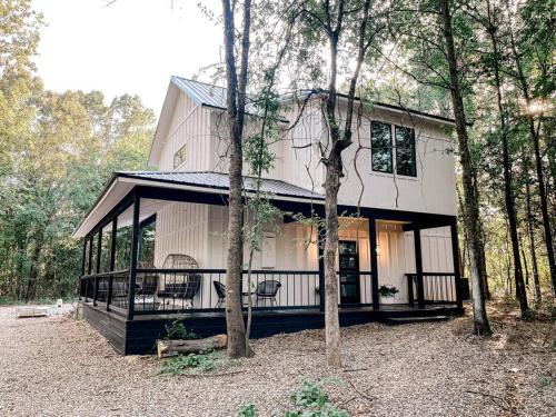a white house with a porch in the woods at the RISER - BRAND NEW Modern Cabin in Broken Bow in Broken Bow