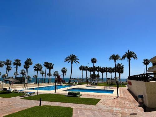 a swimming pool with palm trees and the ocean at Aloha Playa Sol y Mar in Benalmádena
