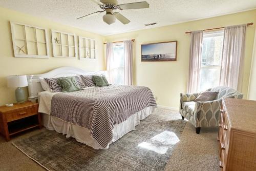 a bedroom with a bed and a chair and windows at Firefly Cottage in Edisto Beach