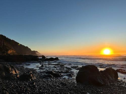 a sunset over the ocean with rocks on a beach at Breakers - stay in a tiny home on the Oregon Coast in Waldport