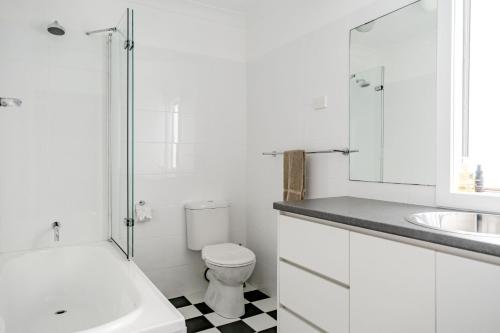 a white bathroom with a toilet and a sink at Bannister Head Beach House in Narrawallee