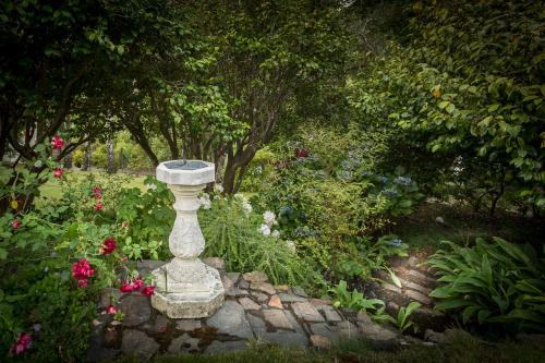 a stone birdbath in a garden with flowers and trees at Beaufort House Akaroa in Akaroa