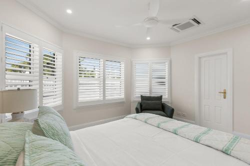 a white bedroom with a bed and a chair at Sandscapes Sanctuary in Broome