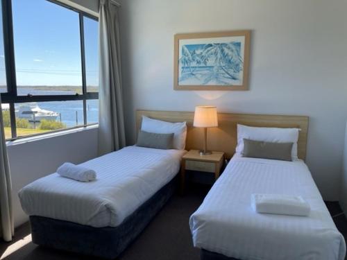 two beds in a hotel room with a window at The Boathouse Luxury Apartments in Tea Gardens