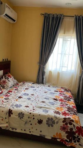 a bedroom with a bed with a floral comforter and a window at SHORT Rental in Ilorin