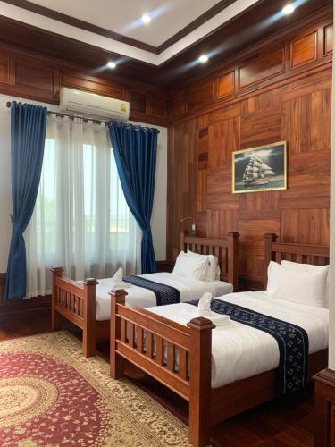 two beds in a room with wooden walls and blue curtains at HotelLaoMixay in Savannakhet