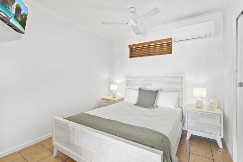 a white bedroom with a bed and a night stand at Sunset Oasis in Airlie Beach