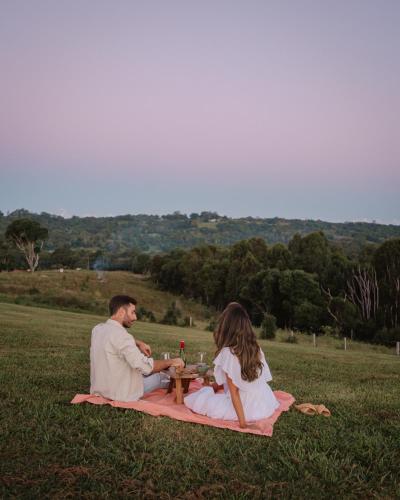 a man and woman sitting on a blanket in a field at Heartwood Farm Byron Bay Luxury Farm Stay in Federal