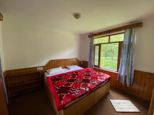 a bedroom with a bed with a red blanket and a window at Double Dutch, Old Manali in Manāli