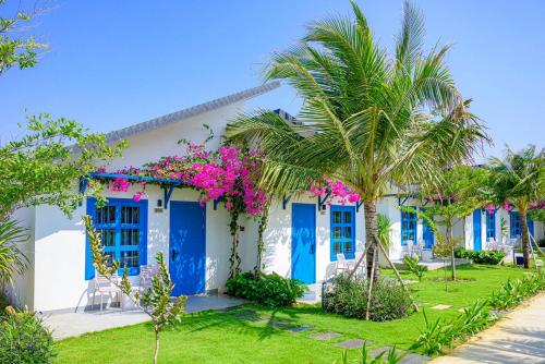 uma casa branca com portas azuis e flores cor-de-rosa em KIGI Beach Resort em Phan Thiet