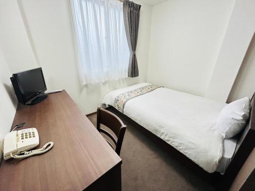 a room with a bed and a desk with a phone at グリーンホテル会津 in Aizuwakamatsu