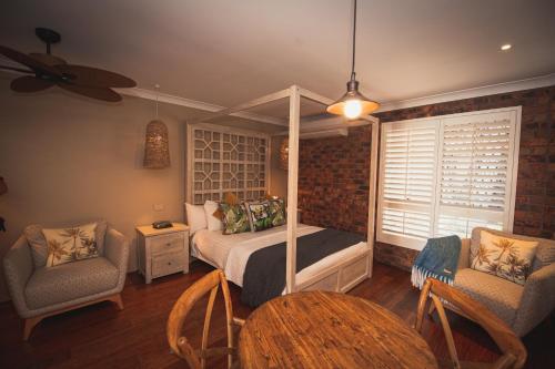 a bedroom with a canopy bed and two chairs and a table at Ballina Palms Boutique Motel in Ballina