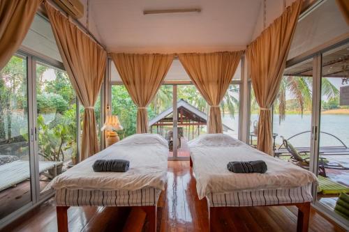 2 camas en una habitación con ventanas grandes en River Flow House (บ้านสายนํ้า), en Ratchaburi