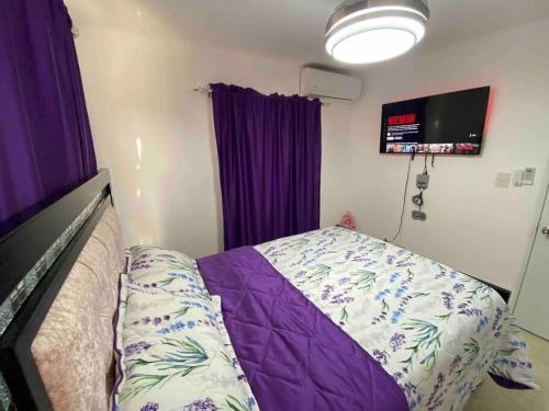 a bedroom with a bed and purple curtains and a tv at Nice and Breezy Apartment in Santiago de los Caballeros