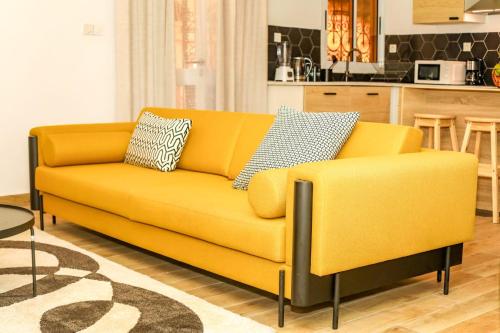 a yellow couch in a living room with a kitchen at Maison Meublée *WIFI* *CLIM* *PARKING* in Douala
