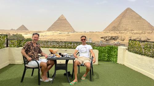 two men sitting at a table in front of the pyramids at Solima pyramids inn in Cairo