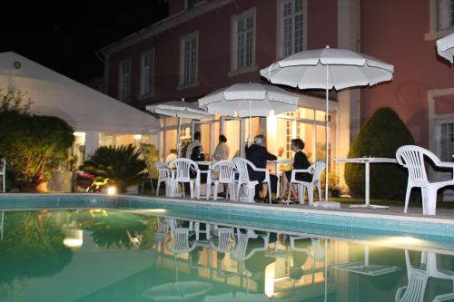 a group of people sitting at a table with umbrellas by a pool at Vila Duparchy in Luso