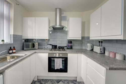 uma cozinha com armários brancos e um forno com placa de fogão em Stunning and Lovely 3 Bed House - Catch 22 em Coventry