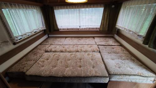 an empty bed in a room with two windows at Zážitkový pobyt v karavanu u Slezské Harty 