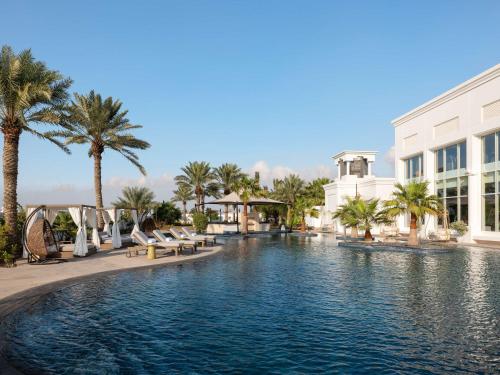 basen w ośrodku z palmami i budynek w obiekcie Raffles Al Areen Palace Bahrain w mieście Manama