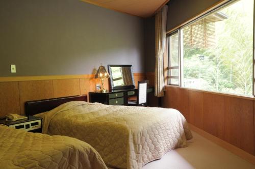 1 dormitorio con 2 camas y ventana en Yugawara Onsen Kawasegien Isuzu Hotel, en Atami