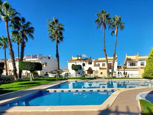 a swimming pool with palm trees in front of a house at Casa Prins 2-bed apartment with stunning views in Ciudad Quesada