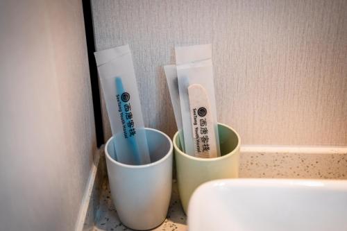two cups with toothbrushes in them next to a toilet at Xi'an See Tang Guesthouse in Xi'an