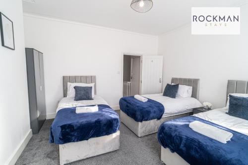 3 Betten in einem weißen Zimmer mit blauer Bettwäsche in der Unterkunft 32 The Grove - Modern & Elegant Home Close to Beach with Parking by RockmanStays in Southend-on-Sea