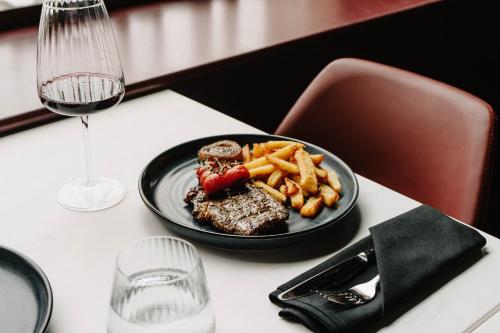 a plate of steak and french fries on a table with a glass of wine at The Halyard Liverpool, Vignette Collection by IHG in Liverpool