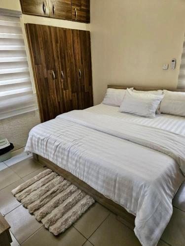 a large white bed in a bedroom with a rug at an exquiste 3 bedroom apartment, in a peaceful environment in Abuja