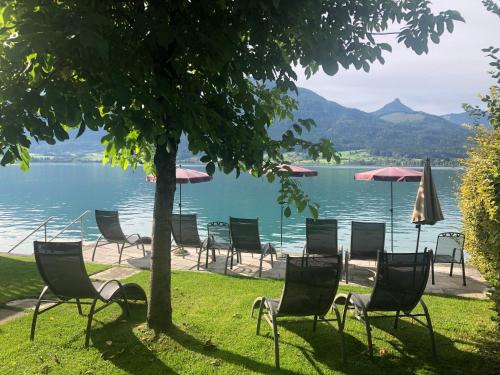 eine Gruppe von Stühlen und Sonnenschirmen auf dem Gras in der Nähe eines Sees in der Unterkunft Hotel Zimmerbräu in St. Wolfgang