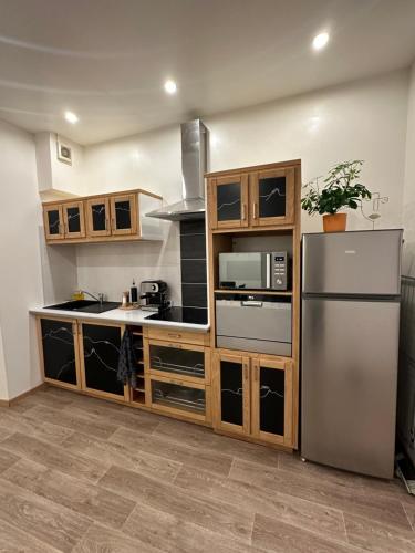 une cuisine avec des armoires en bois et un réfrigérateur en acier inoxydable dans l'établissement Le Refuge T3 centre ville 63m2 pied des montagnes, à Albertville