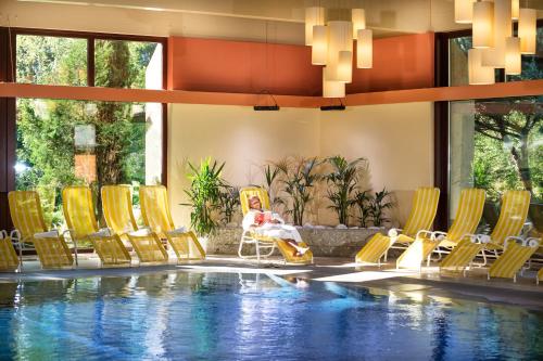 a pool with yellow chairs and a person sitting on a chair next to a pool at Johannesbad Hotel Palace - Kinder bis 11 kostenfrei in Bad Hofgastein