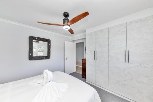 a bedroom with a white bed with a ceiling fan at Sea Breeze in Bloubergstrand
