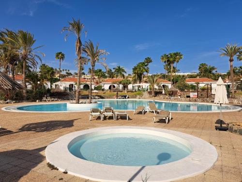une grande piscine avec des chaises et des palmiers dans l'établissement Precioso bungalow en Maspalomas, à San Bartolomé
