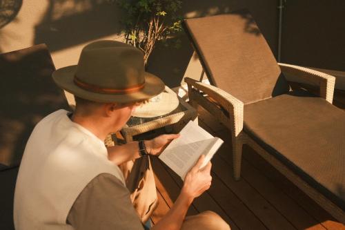 Ein Mann mit Hut, der auf einer Bank sitzt und ein Buch liest. in der Unterkunft Hotel Mühlbacherhof in Algund