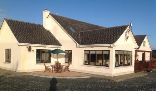 a white house with a table and an umbrella at 4 bedroom holiday home overlooking the sea in Connemara in Rossaveel