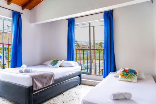 2 camas en una habitación con cortinas azules y ventana en Hotel Villa Guatape, en Guatapé