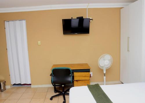 a bedroom with a desk and a television on the wall at Obasi Green Inn Guesthouse in Roodepoort