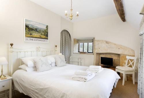 a bedroom with a large white bed and a fireplace at Slatters Cottage - 17th Century Cotswolds Cottage in Bourton on the Hill