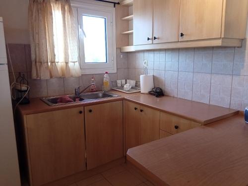eine Küche mit Holzschränken, einem Waschbecken und einem Fenster in der Unterkunft INFO στούντιο in Messini