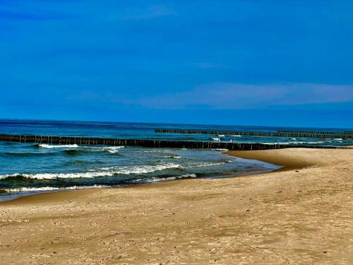a sandy beach with a pier in the ocean at Dom wakacyjny Welle Dziwnów in Dziwnów