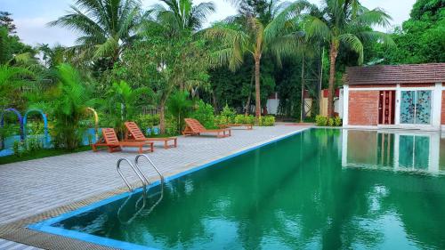 a swimming pool with chairs and a building and palm trees at Kokomo Sunset Resort in Gazipur