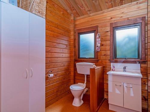 baño con aseo y lavabo y 2 ventanas en Boltons Bach - Whangapoua Bach, en Whangapoua