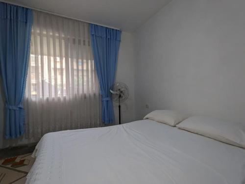 a bedroom with a white bed and blue curtains at Communist style room in Shkodër