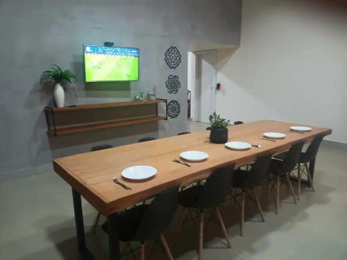 a large wooden table with chairs and a tv on a wall at Casa na fazenda inteira ou quartos individuais no Hostel Recanto da Felicidade Paraopeba in Paraopeba